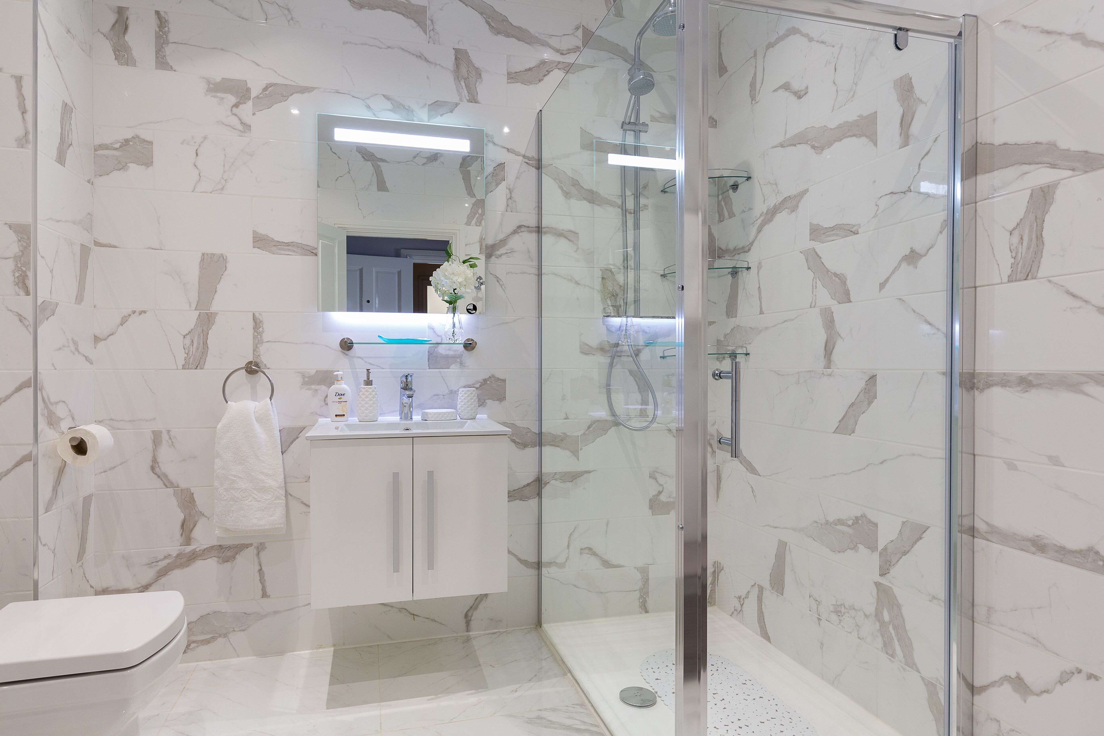 A modern bathroom with a glass-enclosed shower, marble tiles, a white sink, and a toilet.