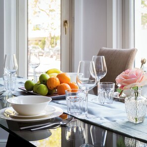 A dining table set with plates, bowls, cutlery, and glasses, with a bowl of fruit and a vase of flowers. - Cromwell Road Apartments (London)