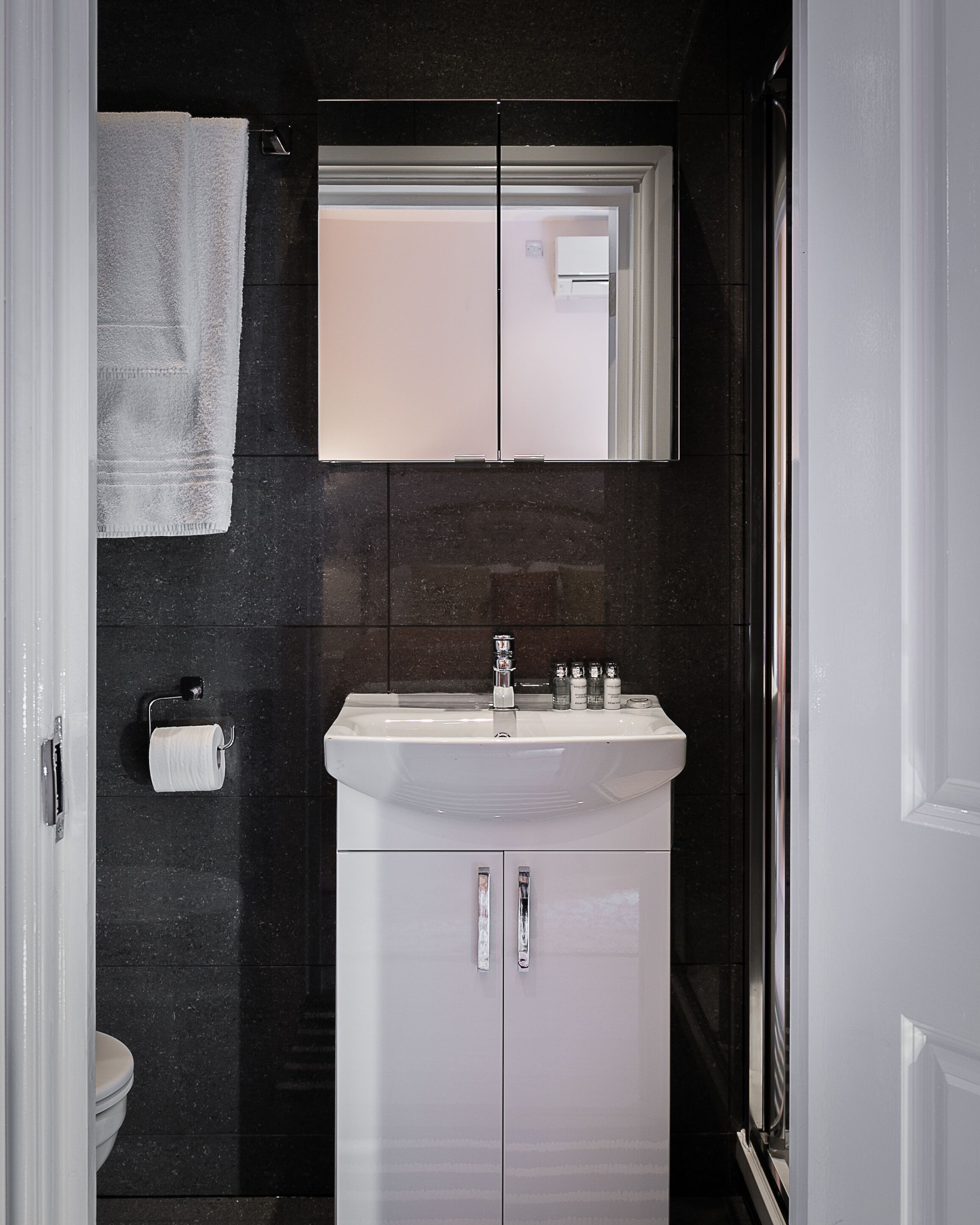 A bathroom with a white sink, two cabinets, a mirror, and a toilet.