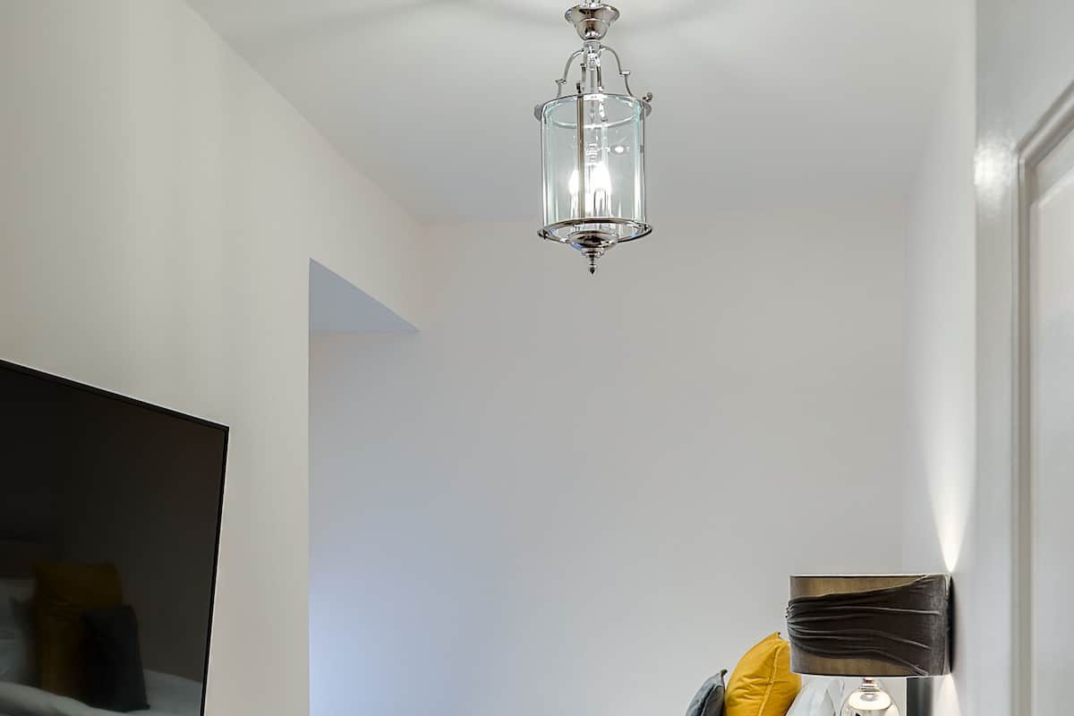 Une chambre à coucher moderne avec un canapé violet, un lit recouvert d’une couverture bleue et un téléviseur fixé au mur.