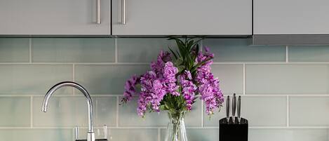 A modern kitchen with grey cabinets, a stainless steel sink, and a vase with purple flowers.