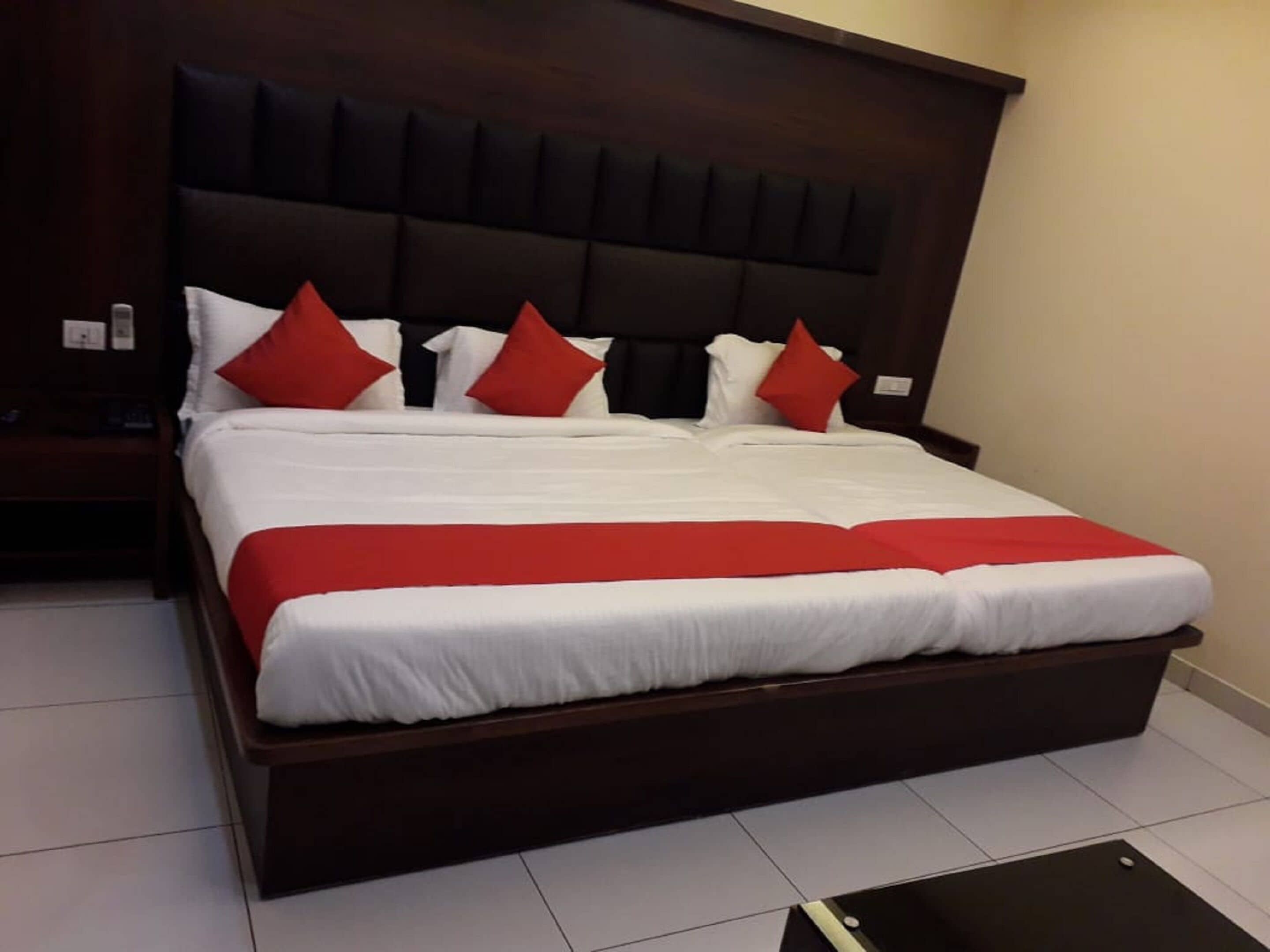 Una cama grande con cabecera de madera, ropa de cama blanca y almohadas rojas.