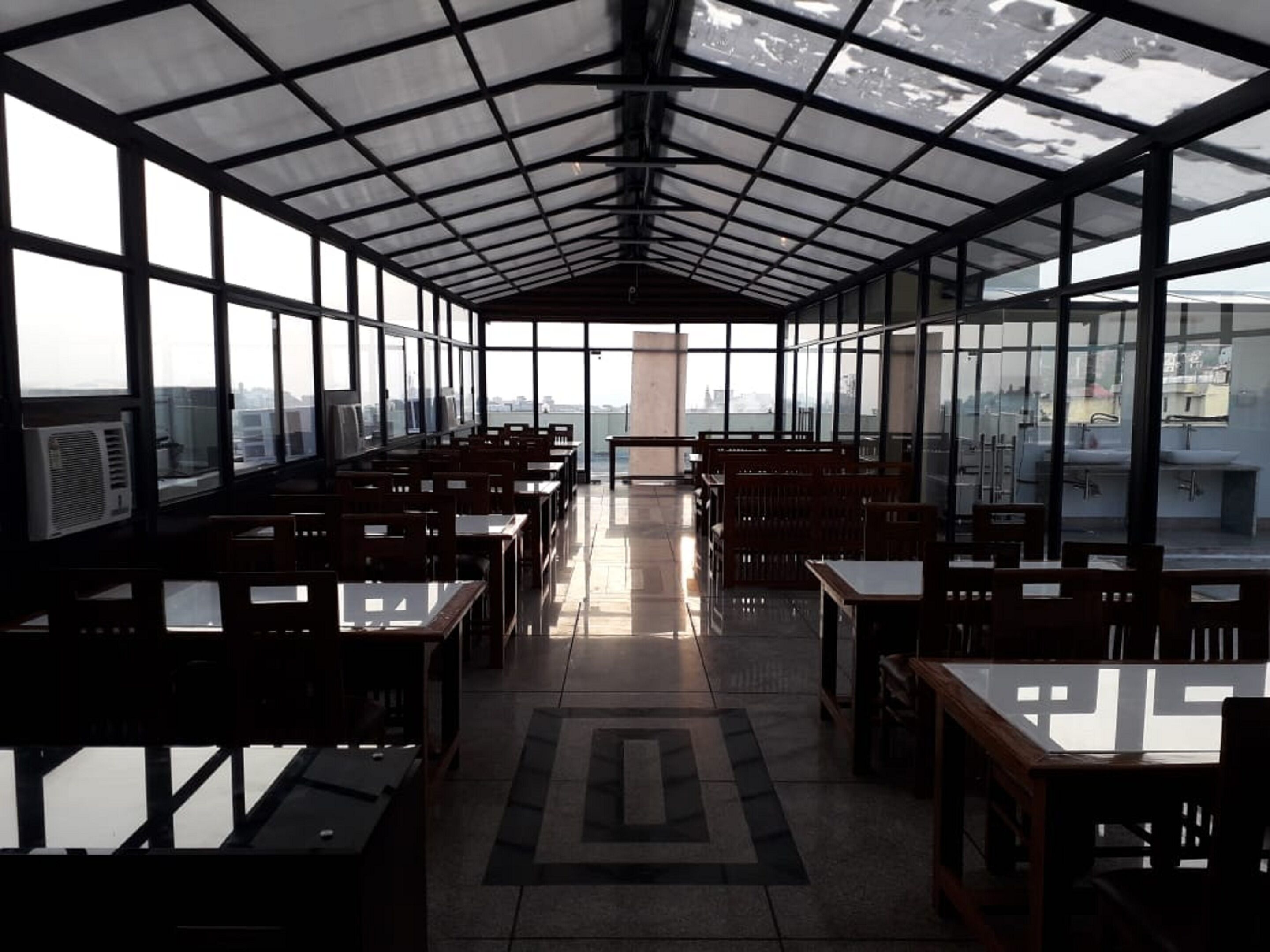 A spacious indoor area with tables and chairs arranged in rows, large windows on the sides, and a view of the cityscape through the windows.