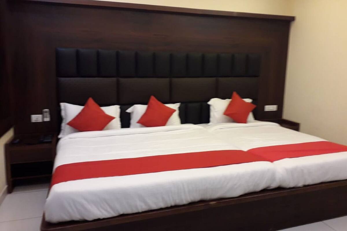 Una habitación de hotel con una cama grande, cabecera de madera oscura, ropa de cama blanca y almohadas rojas.