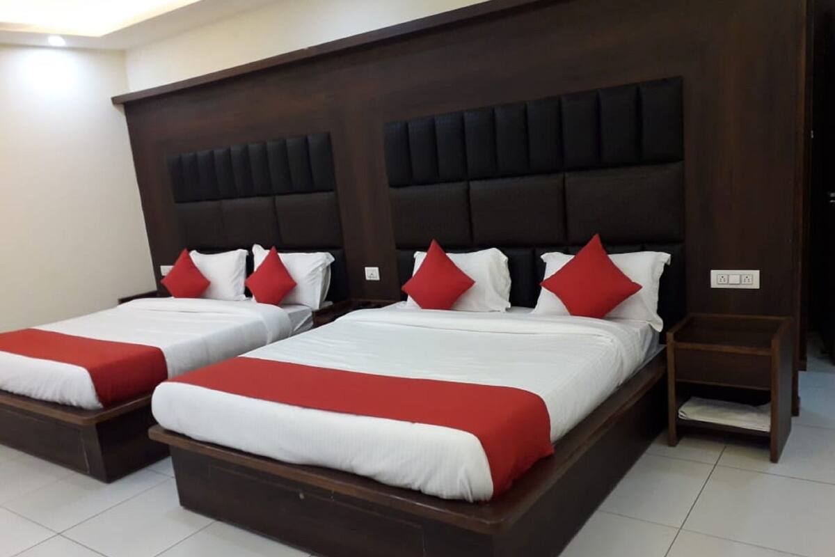 Habitación de hotel con dos camas, cada una con cabecera de madera, ropa de cama blanca y detalles en rojo.
