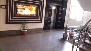 A spacious lobby with a large framed artwork, a potted plant, and a staircase leading to an upper level. - Hotel Royal Stay (Reasi)