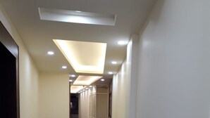 A long, narrow hallway with a polished floor, recessed lighting, and potted plants. - Hotel Royal Stay (Reasi)