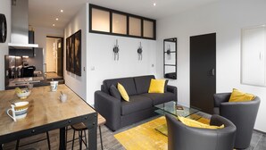 Una sala de estar moderna con un sofá, sillones, una mesa de centro de vidrio y un comedor con mesa y sillas de madera.