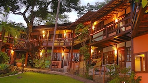A multi-story building with balconies, a covered outdoor seating area, and a well-maintained garden. - Pousada Villa da Prainha (Ilhabela)