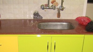 Una cocina con un lavamanos, armarios amarillos y salpicadero de azulejos con motivos de frutas.