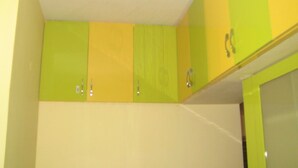 Una cocina con gabinetes verdes y amarillos, paredes blancas y techo blanco.