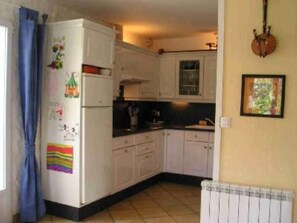 Cocina compacta con armarios blancos, un refrigerador y piso de baldosas.