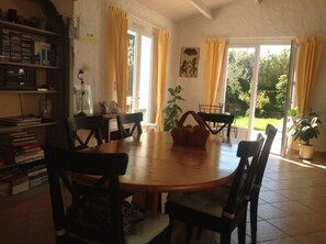 Un comedor con una mesa redonda de madera, seis sillas, una estantería y un ventanal con cortinas.