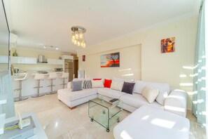 A modern living room with a sectional sofa, a glass coffee table, and a kitchen area in the background. - 2 bed/2 bath - Own private pool, large outdoor space. Very central (Kalkan)