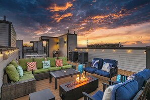 A rooftop patio with outdoor seating, a fire feature, and city views at sunset.