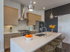 Una cocina moderna con una isla central, electrodomésticos de acero inoxidable e iluminación colgante.