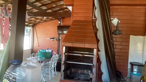 A rustic outdoor seating area with a brick oven, white metal chairs, and a table with cleaning supplies.