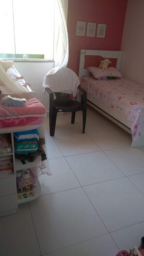 A child's bedroom with a bed, a chair, and a shelf with various items.