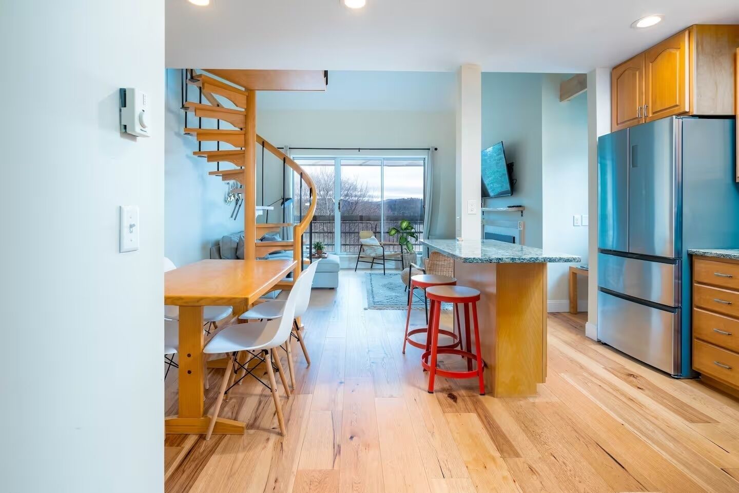Een moderne keuken met een houten eettafel, barstoelen, een vast geïnstalleerd kookeiland en een roestvrijstalen koelkast.