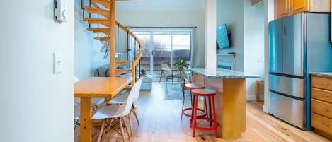 A modern kitchen with a wooden dining table, bar stools, a built-in island, and a stainless steel refrigerator.