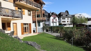 A residential building with a balcony, a small garden area, and a view of the surrounding neighborhood. - Petit Nid Douillet au Coeur de Salvan (Salvan)