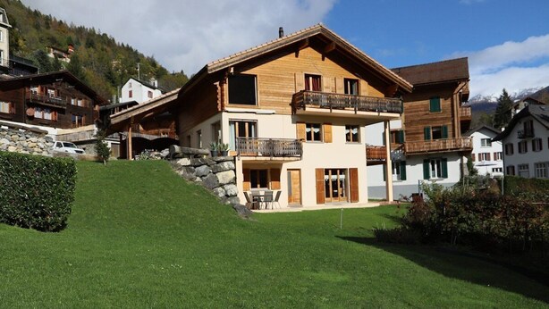A multi-story wooden chalet with balconies, a stone foundation, and a grassy slope. - Petit Nid Douillet au Coeur de Salvan (Salvan)