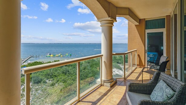Een balkon met uitzicht op zee, een eethoek met stoelen en een glazen deur die naar een kamer leidt.