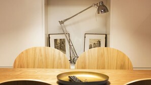 Ein Esstisch mit einer Fernbedienung, zwei Stühlen, einer Schreibtischlampe und zwei gerahmten Bildern an der Wand.