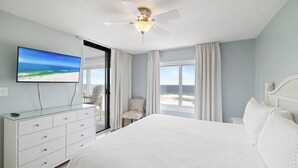 A bedroom with a bed, a TV, a dresser, a chair, and a ceiling fan.