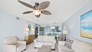A living room with a ceiling fan, two sofas, a coffee table, and a dining area in the background.