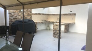 Un espace extérieur aménagé en terrasse, doté d’un coin salon couvert, d’un barbecue et d’un comptoir de cuisine.
