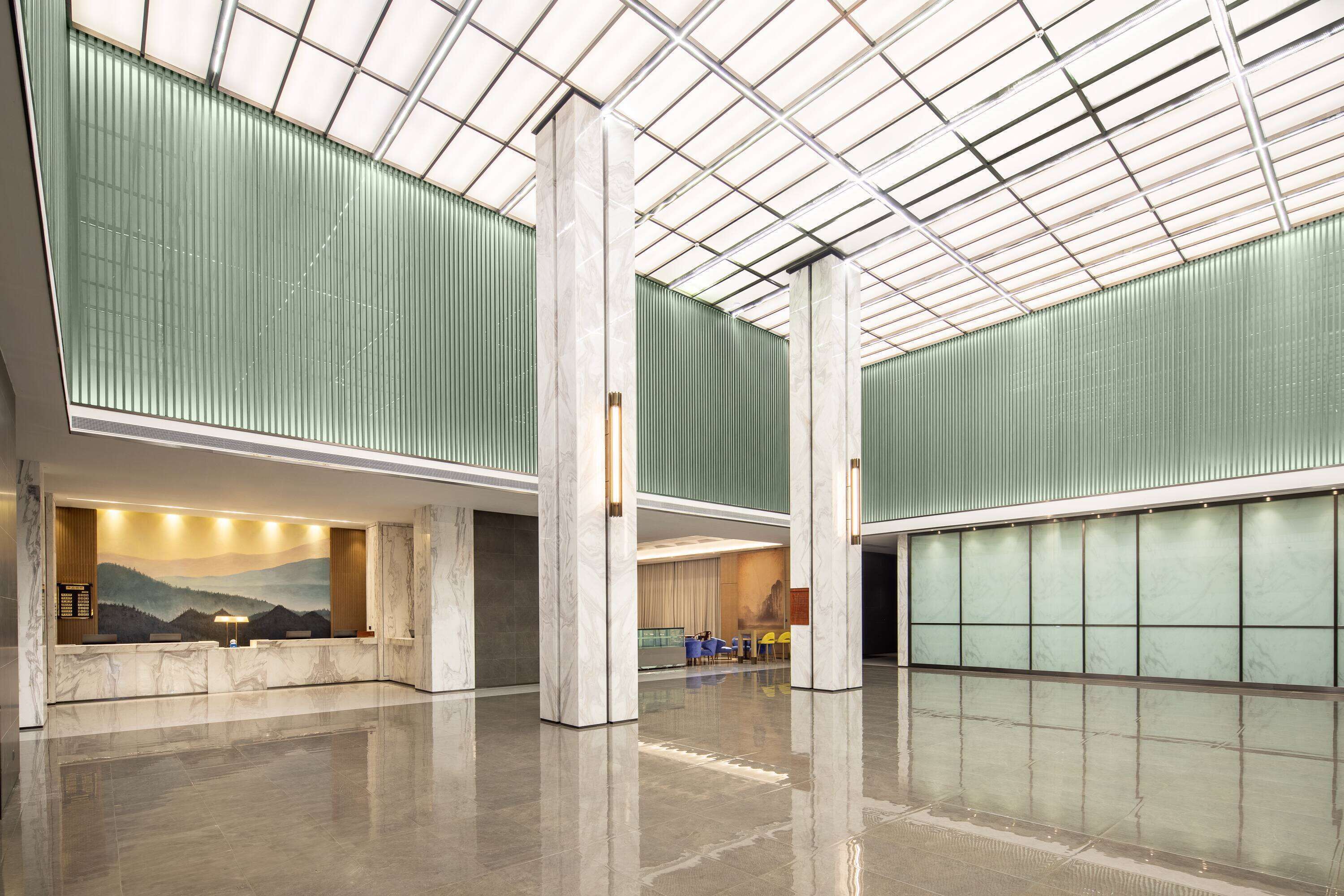 Un vestíbulo amplio con techo alto, ventanas grandes y una zona de recepción con un mural.
