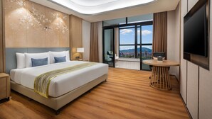Habitación de hotel moderna con una cama grande, un escritorio, un televisor y un balcón con vista a la ciudad.