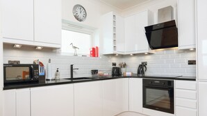A modern kitchen with white cabinets, a black microwave, a sink, and a stove. - 1 Lyndhurst (Salcombe)