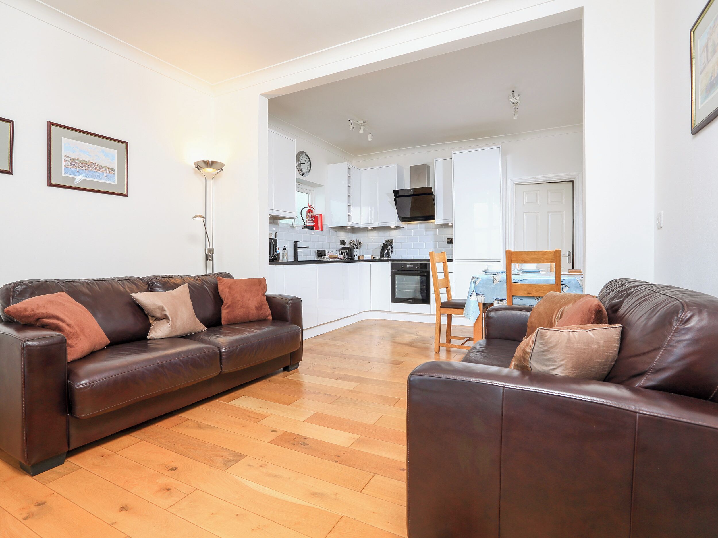 A modern living room with a brown leather sofa, a wooden dining table, and a kitchen in the background.