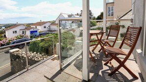 A balcony with a glass door, wooden chairs, and a view of houses and a road. - 1 Lyndhurst (Salcombe)