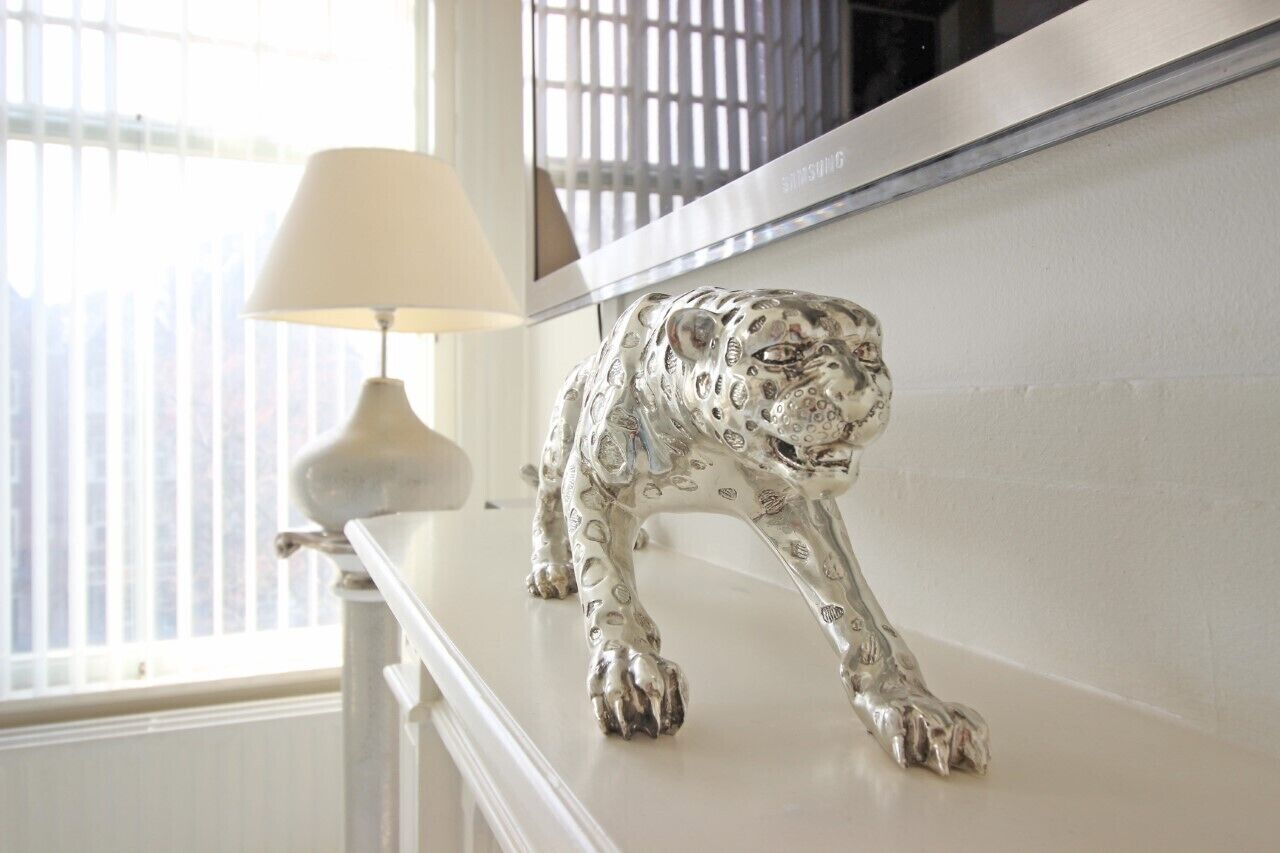 Una estatua de leopardo sobre una consola blanca cerca de una ventana con persianas.