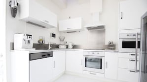 Una cocina moderna con armarios blancos, lavavajillas, horno, cafetera y hervidor.