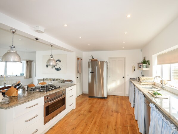 A spacious kitchen with a central island, stainless steel appliances, and wooden flooring.