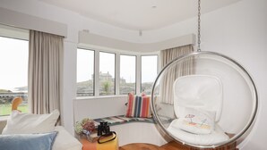 Una habitación moderna con un ventanal grande, un sillón de vidrio redondo, un sofá y suelo de madera.