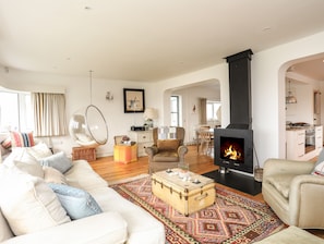 A living room with a sofa, armchairs, a hanging chair, a fireplace, and a dining area with a table and chairs. - Angorfa - Trearddur Bay (Holyhead)