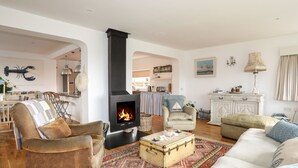 Una sala de estar acogedora con chimenea, asientos cómodos y una cocina al fondo.