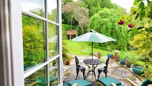 Un pati amb taula i cadires, envoltat de plantes en testos i vista cap a un jardí frondós.