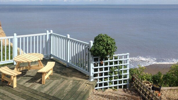 Una terraza de madera con mesas de picnic con vistas a la playa.