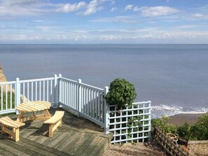 Una terraza de madera con mesas de picnic con vistas a la playa.