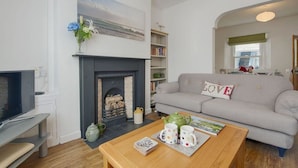 Una sala de estar con chimenea, un sofá gris, un televisor y una mesa de centro con tazas.