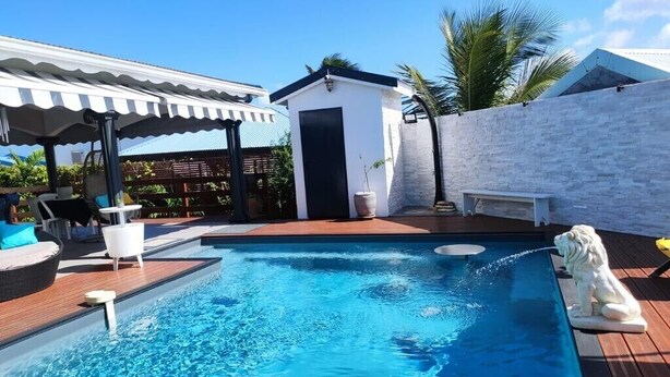 Une piscine avec une terrasse en bois, des chaises longues et un petit bâtiment blanc.