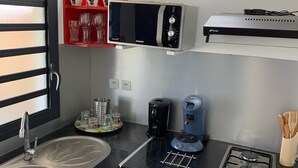 Une cuisine compacte équipée d’un évier, de placards rouges, d’un four à micro-ondes, d’une machine à café et d’une cuisinière à gaz.