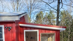 Una cabaña roja de madera con puerta, ventana y un muelle de madera que conduce a la entrada.