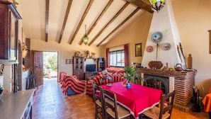 A cozy living room with a fireplace, wooden beams, a dining area with a red tablecloth, and a TV. - Villa Calena Almuñécar by Ruralidays (Granada)